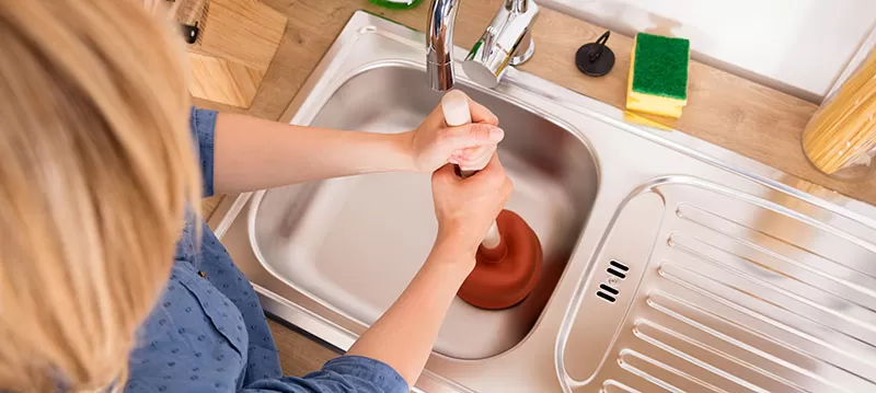 woman using plunger blocked kitchen sink unclog drain