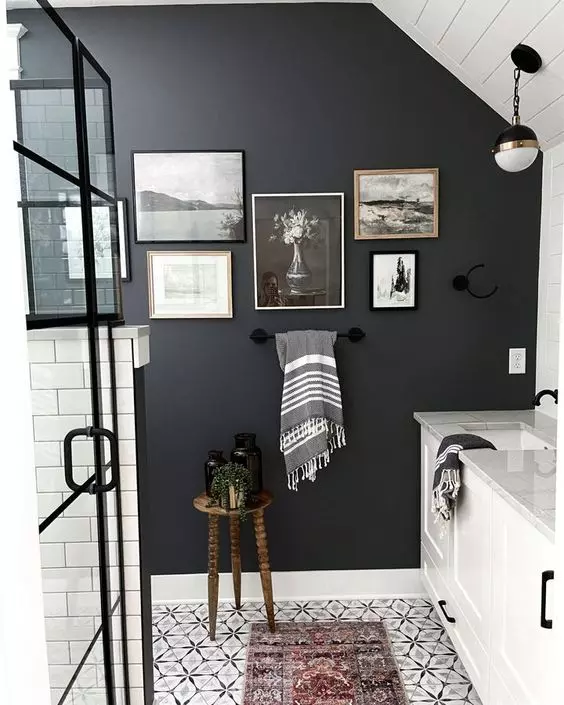 a black and white bathroom with a black accent wall a monochromatic gallery wall white furniture and a shower space done with white subway tiles